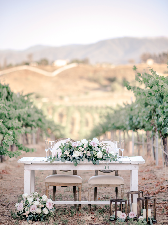 Sweetheart table in the middle of the vines at a winery with wedding bouquets and wood lanterns